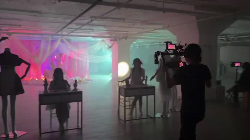 Music video set with camera crew filming performers in colored light